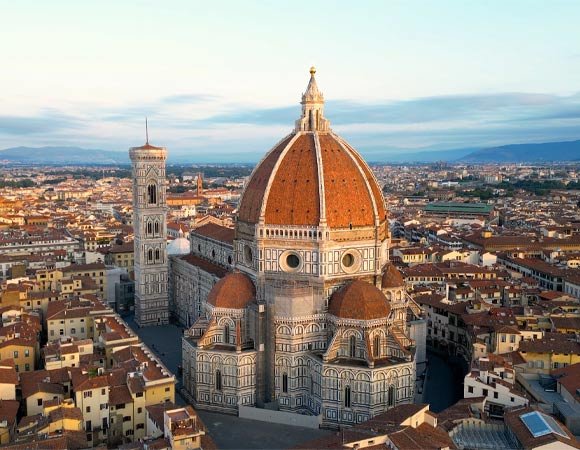 Aerial view of Florence’s Cathedral of Santa Maria del Fiore featuring Brunelleschi’s red-tiled dome and Giotto’s Campanile rising above the terracotta-roofed cityscape under soft morning light